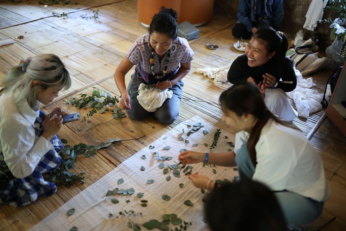 Visitors laying leaves on cloth at an eco-print workshop on the bamboo floor