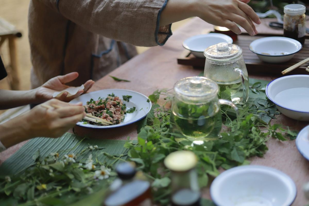 Hands sharing food, herbs and tea across a long table